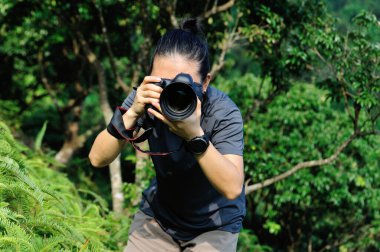 Profesyonel dijital kamerayla yeşil ormanda fotoğraf çeken bir fotoğrafçı.
