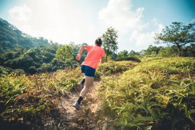 Tropikal ormanda ultra maraton antrenmanı yaparken bir kadın dağ yamacında koşuyor.