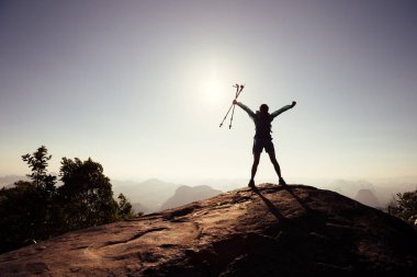 Sırt çantalı tezahüratçı kadın dağların tepesinde güneşin doğuşunun tadını çıkarıyor.