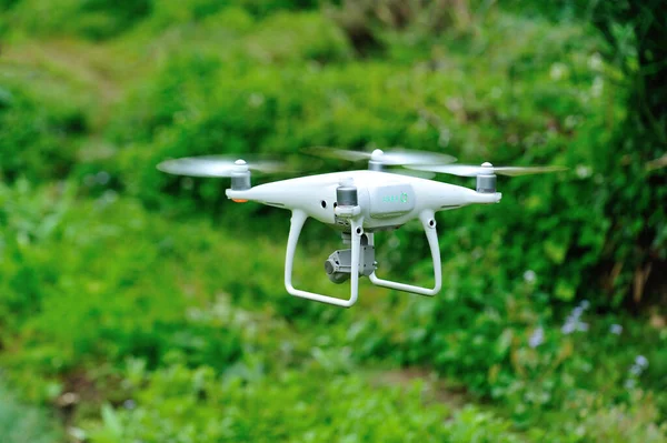 White drone with camera flying in green countryside