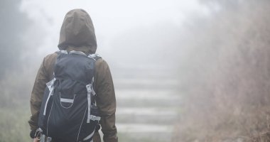 Sisli dağın tepesinde, patikada yürüyen kadın yürüyüşçü.