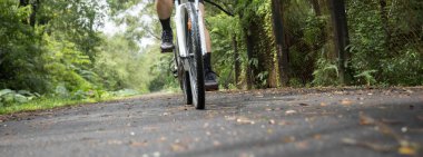 Yazın güneşli park yolunda bisiklet süren bisikletçilerin alt kesimi.