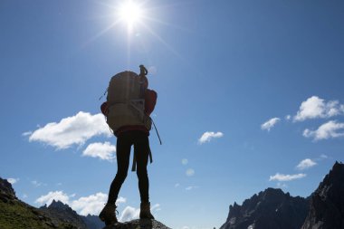 Sırt çantalı başarılı bir kadının silueti gün doğumunda dağın tepesinde yürüyüş yapıyor.