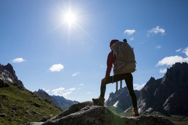 Sırt çantalı başarılı bir kadının silueti gün doğumunda dağın tepesinde yürüyüş yapıyor.