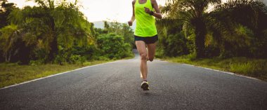 Genç, formda bir kadın tropik orman yolunda koşuyor.