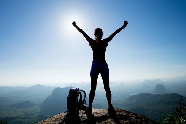 Cheering female backpacker enjoying view on sunrise mountain top cliff edge