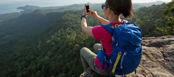 女性ハイカーは山の頂上でスマートフォンで写真を撮る — ストック写真