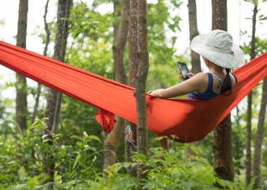 Hamakta dinlenen bir kadın yağmur ormanlarında akıllı telefon kullanıyor.