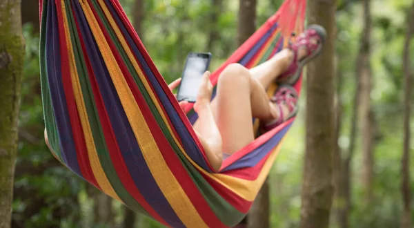 熱帯雨林のスマートフォンでハンモックでリラックスした女性 — ストック写真