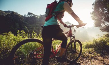 Genç bisikletçi yaz ormanı patikasında güzel gündoğumunun tadını çıkarıyor.