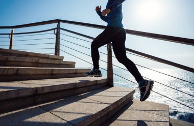 Spor salonundaki kadın koşucu deniz kenarındaki merdivenlerde koşuyor.