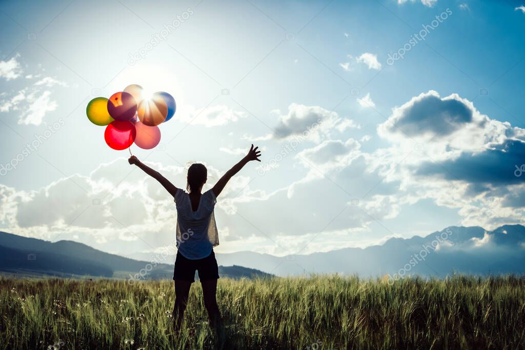 Cheering young woman standing on grassland with colored balloons