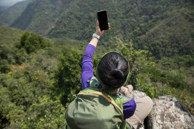 Dağın tepesinde akıllı telefon kullanan başarılı bir yürüyüşçü.
