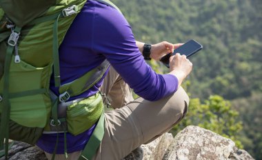 Dağın tepesinde akıllı telefon kullanan başarılı bir yürüyüşçü.