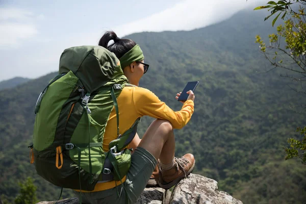 成功的徒步旅行者在山顶悬崖边使用智能手机 — 图库照片