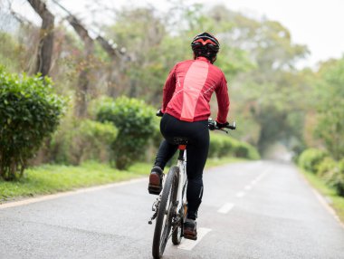 Baharda güneşli park yolunda bisiklet süren bir kadın bisikletçi.