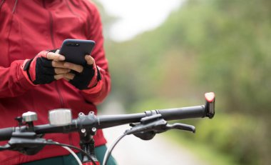 Bisikletçi orman yolunda dağ bisikleti sürerken akıllı telefon kullanır
