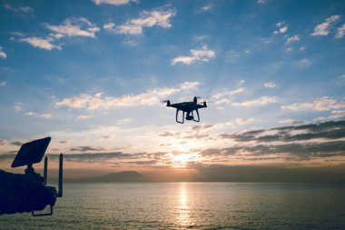 Uzaktan kumandalı siluet güneş doğarken deniz üzerinde fotoğraf çeken uçan bir dron.
