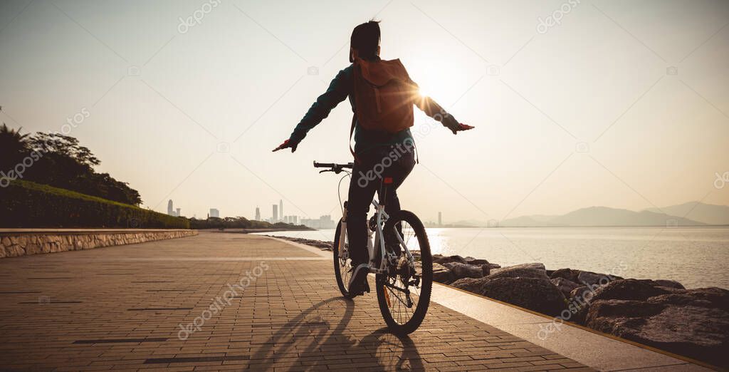 Female cyclist hands free cycling riding bike with arms outstretched in the coasts sunrise 