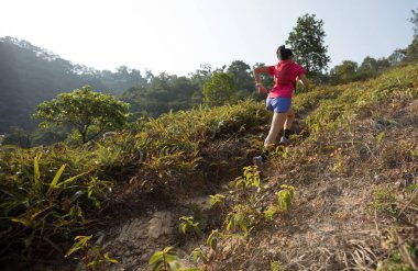 Tropikal ormanda dağ yamacında koşan bir kadın koşucu.