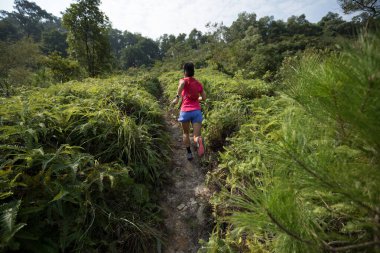 Tropikal ormanda dağ yamacında koşan bir kadın koşucu.