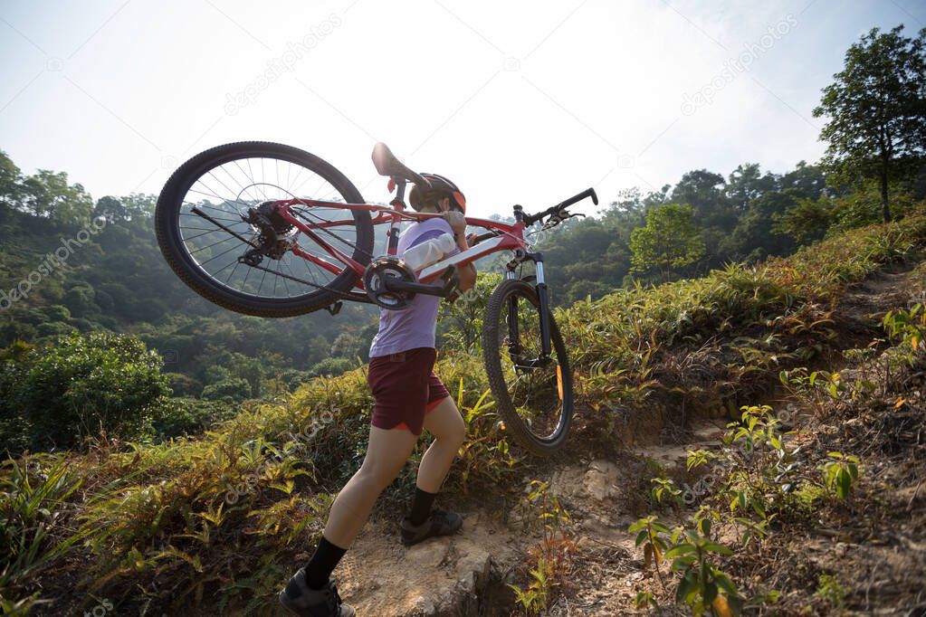 Cross country biking woman cyclist with mountain bike climbing up the mountain slope on tropical forest trail