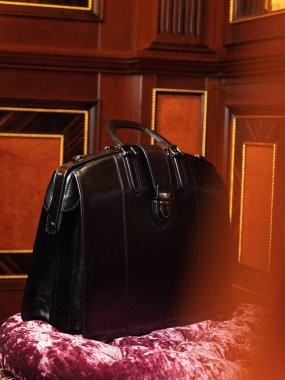 Zengin bir ofiste kadife bir sandalyede oturan siyah bir adamın iş çantası.