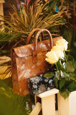 Çok renkli kahverengi deri bir evrak çantası ve çiçekler arasında güller var.
