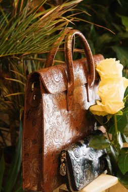 Çok renkli kahverengi deri bir evrak çantası ve çiçekler arasında güller var.