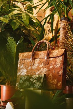 Çok renkli kahverengi deri bir evrak çantası ve çiçekler arasında güller var.