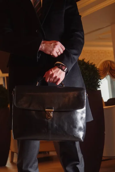 Un hombre en un traje de negocios y abrigo largo con un maletín de cuero negro en un centro de negocios — Foto de Stock