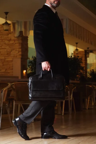 Un hombre en un traje de negocios y abrigo largo con un maletín de cuero negro en un centro de negocios — Foto de Stock