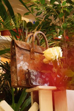 Çok renkli kahverengi deri bir evrak çantası ve çiçekler arasında güller var.