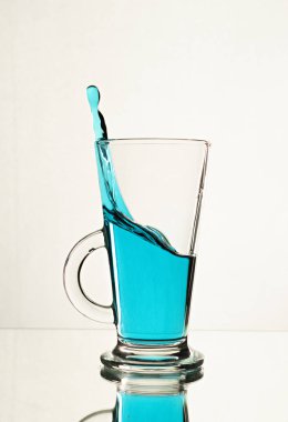 Bir bardak çaya mavi alkol damlatıyor.