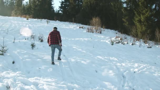 Brutal skogshuggare går längs en snöig sluttning med en yxa — Stockvideo