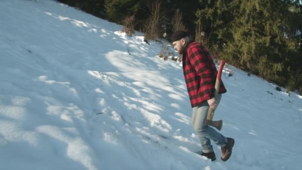 Brutal lumberjack goes along a snowy slope with an ax — Stock Video