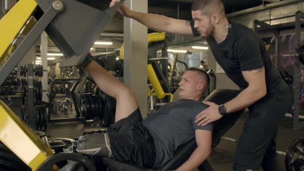 Hombre joven con prótesis de pierna usando máquina de prensa de piernas en el gimnasio — Vídeo de stock