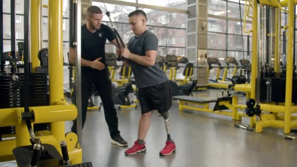 Gehandicapte jongeman met instructeur aan het sporten in de sportschool — Stockvideo