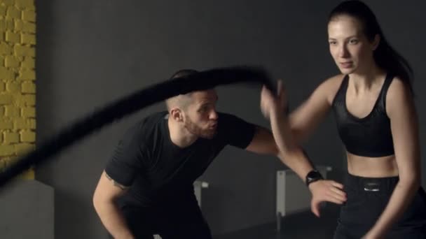 Молодая женщина с инструктором использует боевые веревки в тренажерном зале — стоковое видео