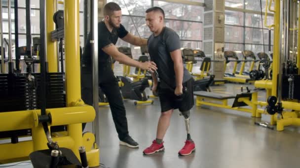 Gehandicapte jongeman met instructeur aan het sporten in de sportschool — Stockvideo