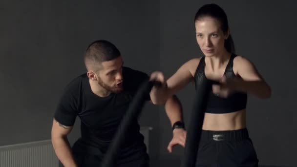 Mujer joven con instructor usando cuerdas de batalla en el gimnasio — Vídeos de Stock