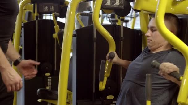 Joven con instructor haciendo ejercicio en el gimnasio — Vídeos de Stock