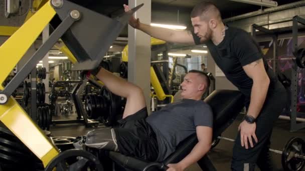 Hombre joven con prótesis de pierna usando máquina de prensa de piernas en el gimnasio — Vídeos de Stock