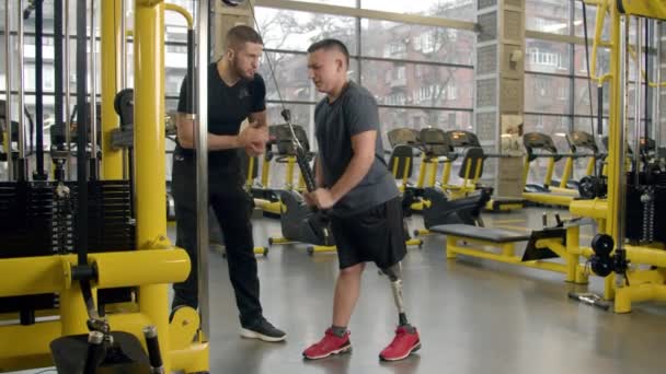 Zdravotně postižený mladý muž cvičit s pomocí instruktora v tělocvičně — Stock video