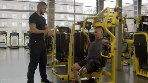 Jovem deficiente com instrutor trabalhando no ginásio — Vídeo de Stock