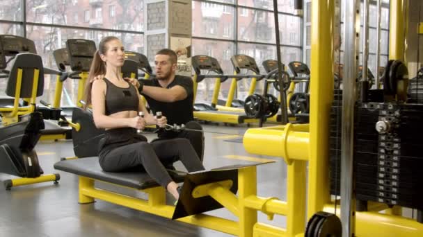 Mujer joven con instructor haciendo ejercicio en el gimnasio mediante el uso de la máquina de remo — Vídeo de stock