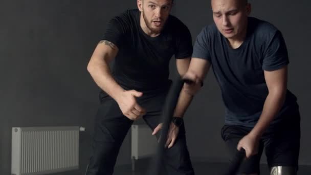 Young man with instructor using battle ropes in gym — Stock Video