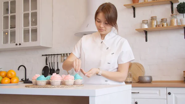 Mujer joven decorando cupcakes en cocina luminosa — Foto de Stock