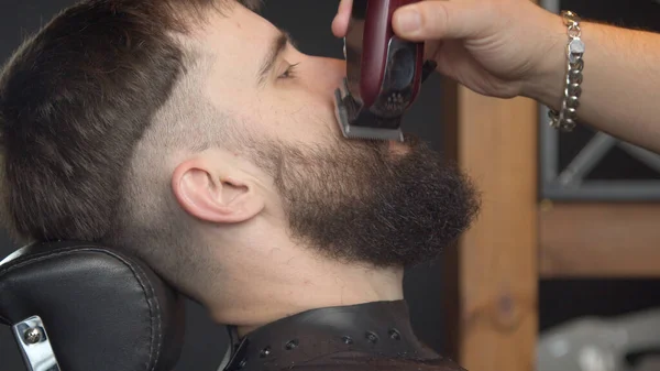 Młody fryzjer strzyże brodę męskiego klienta — Zdjęcie stockowe
