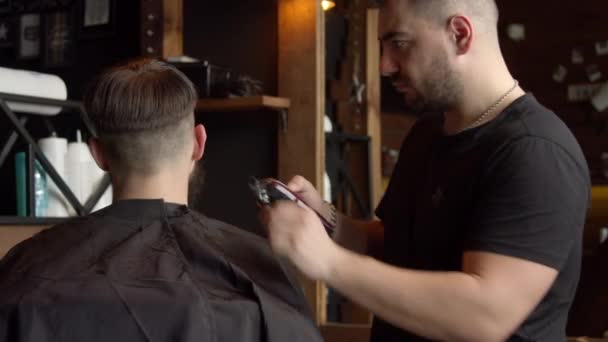 Парикмахер стрижет волосы клиента-мужчины — стоковое видео